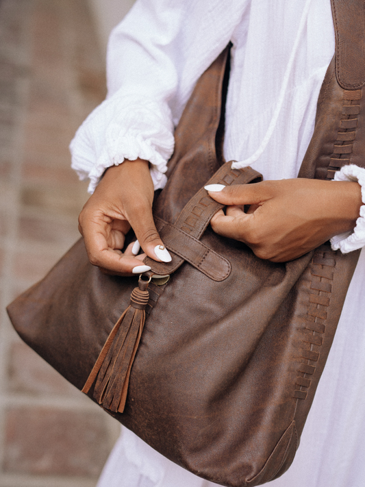A picture showing the detail of Ella Hobo Bag, how it close fitly with the tassel and magnet closure. The hand's model shows how to close and the detail of the handwoven detail. It is Ella Hobo bag from Seminyak Leather Bali.