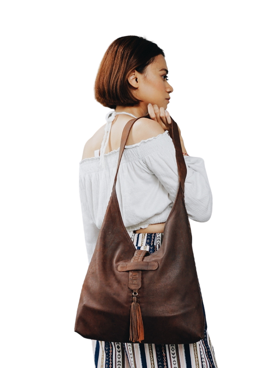A picture shows a model in white blouse hold a bag in her shoulder. It is Ella Hobo Bag from Seminyak Leather Bali. 
