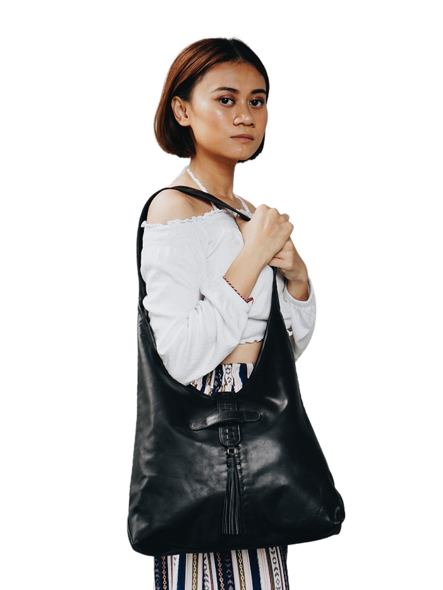 A picture shows a model in white blouse hold a bag in her shoulder. It is Ella Hobo Bag in Black from Seminyak Leather Bali.