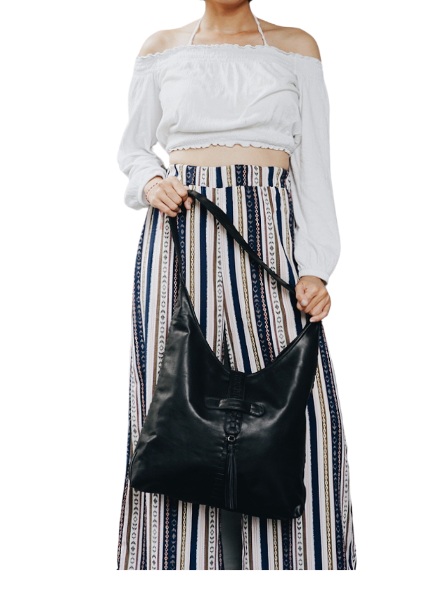 A model with white blouse holding a black bag from Seminyak Leather. The model shows how strong the strap you can put your to go things nicely. It is Ella Hobo Bag.