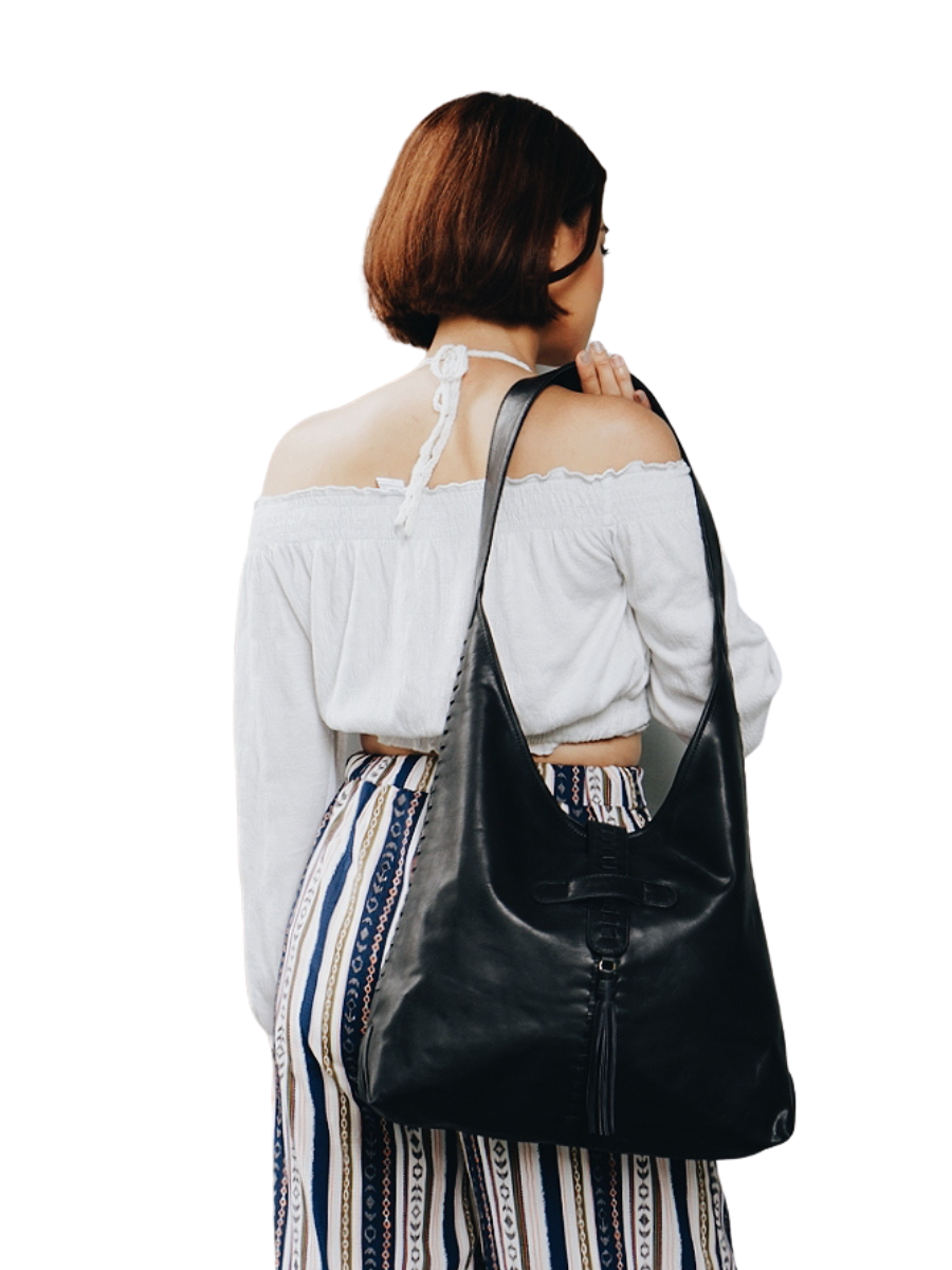 A picture shows a model in white blouse hold a bag in her shoulder. It is Ella Hobo Bag in Black from Seminyak Leather Bali.