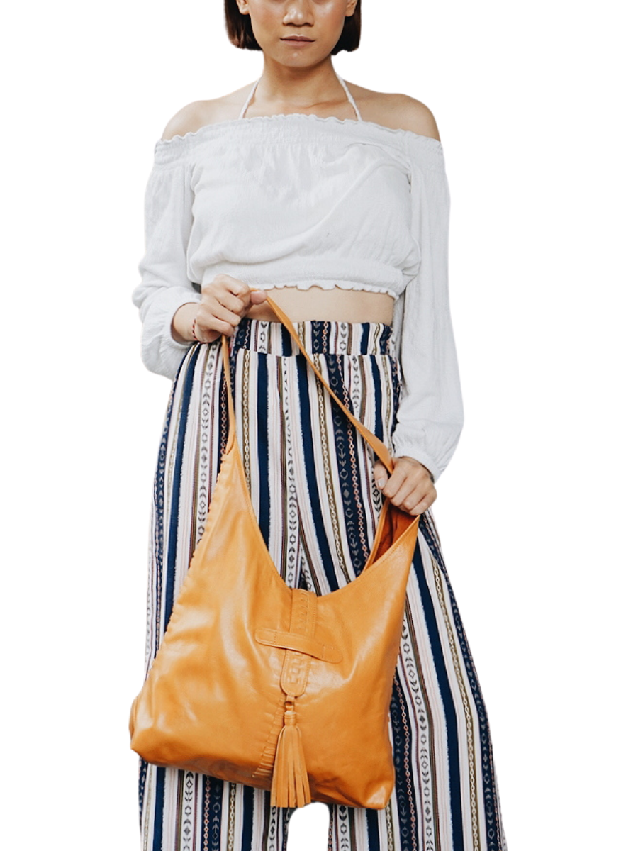 A model with white blouse holding a honey tan bag from Seminyak Leather. The model shows how strong the strap you can put your to go things nicely. It is Ella Hobo Bag.