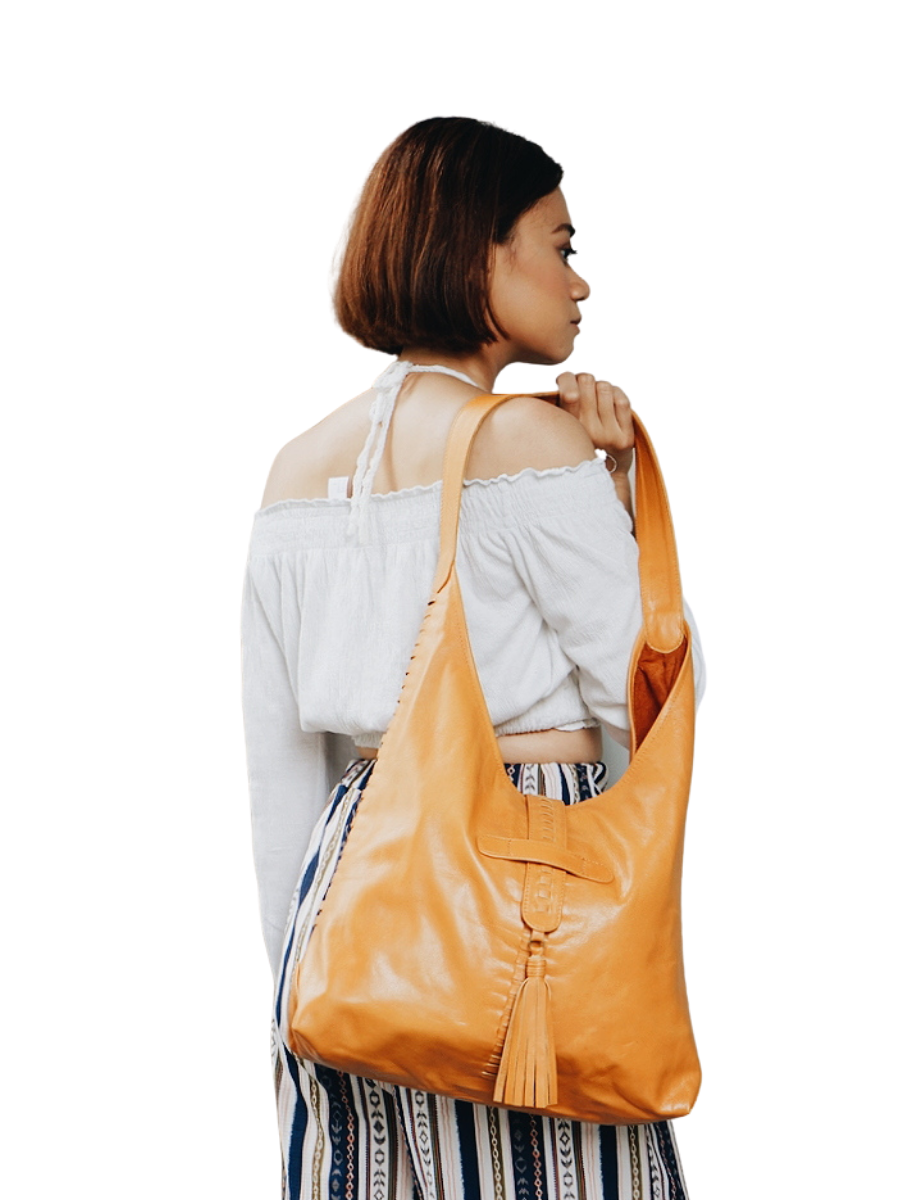 A picture shows a model in white blouse hold a bag in her shoulder. It is Ella Hobo Bag in Honey Tan from Seminyak Leather Bali.