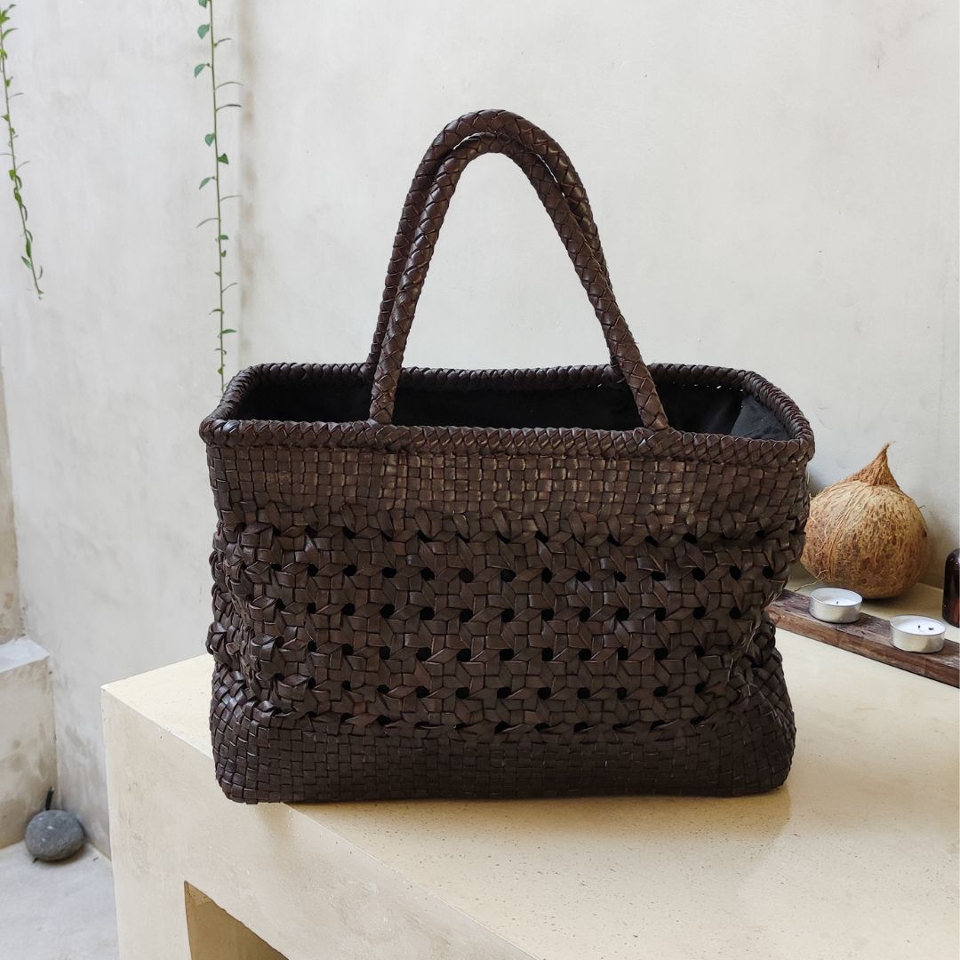 A dark tan medium-sized rectangle handbag made of hand-weaved leather with braided handle and chick-eye weave on the body by Seminyak Leather Bali. A blend of modern elegance and artisanal charm, crafted with meticulous attention to detail.
