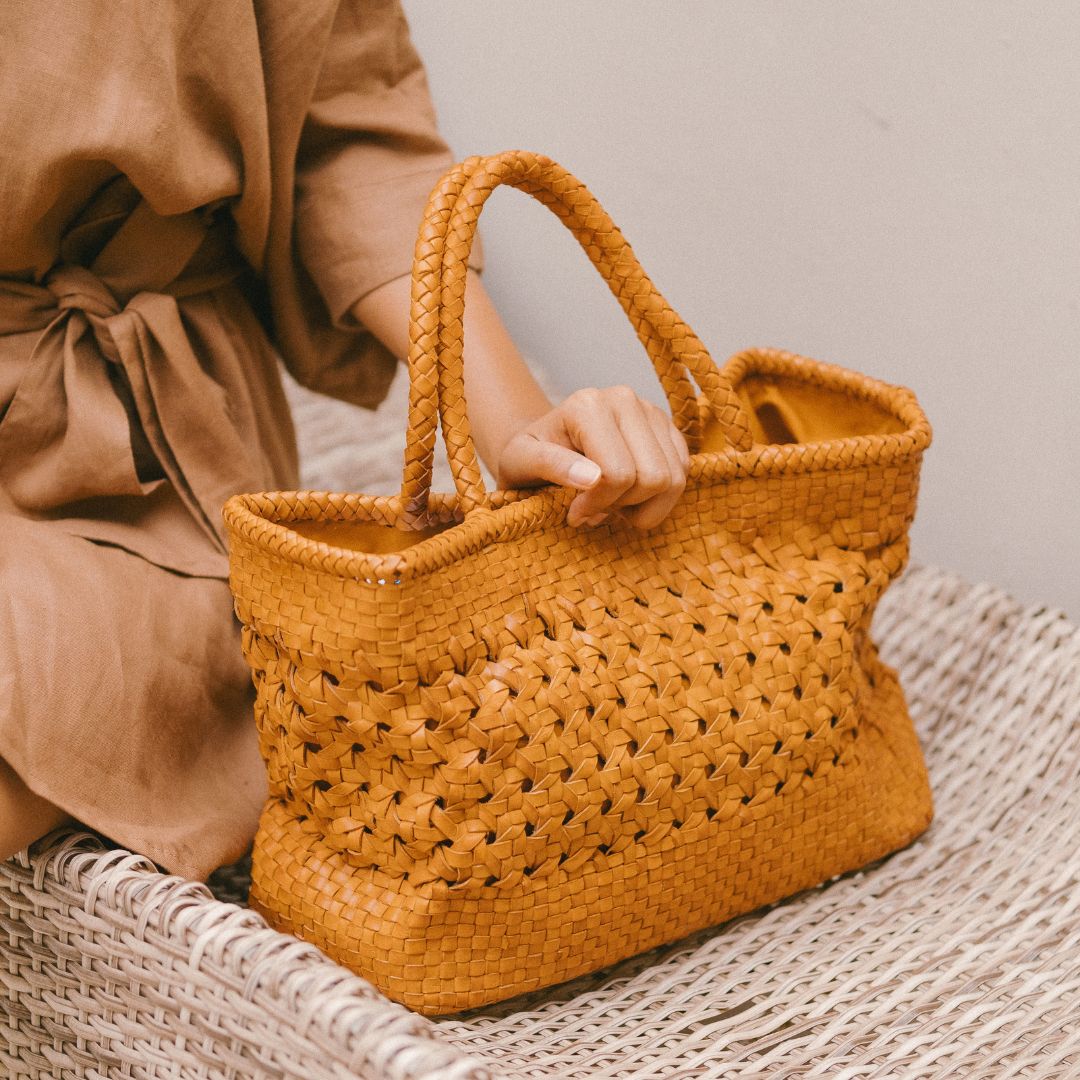A woman hold tan medium-sized rectangle handbag made of hand-weaved leather with braided handle and chick-eye weave on the body by Seminyak Leather Bali. A blend of modern elegance and artisanal charm, crafted with meticulous attention to detail.