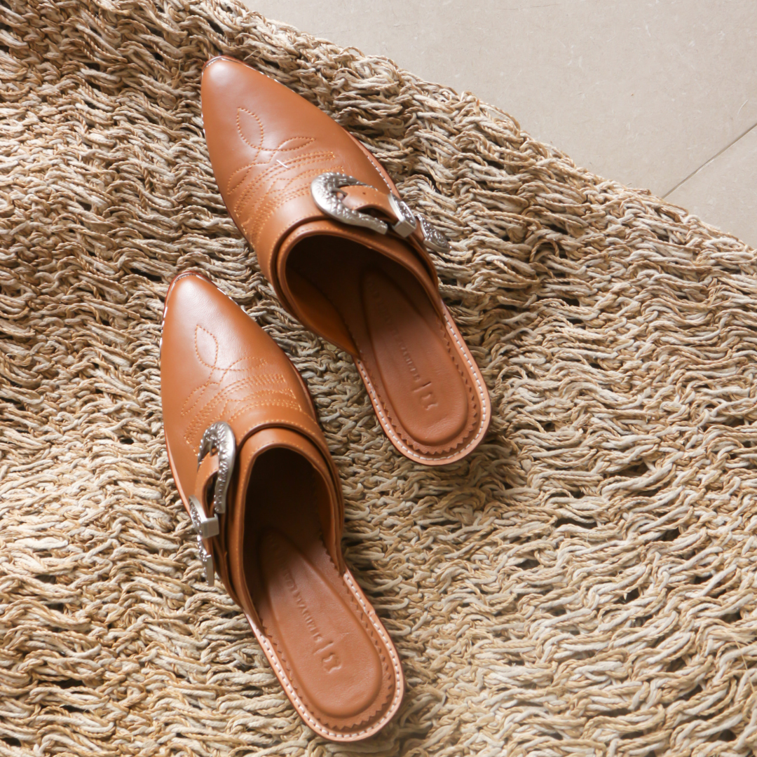 Brown pointy toe mules by Seminyak Leather Bali with western-style stitching on vamp and carved metal toe cap and carved buckle. 5 cm wooden Cuban heel in a natural finish. A blend of Western charm and contemporary elegance, all made of leather.