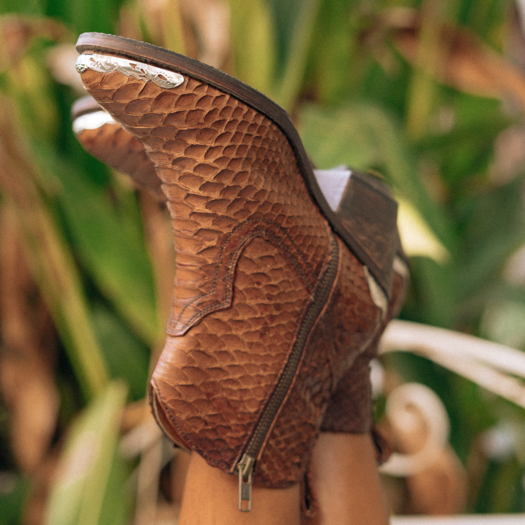Ankle boots by Seminyak Leather Bali made of snakeskin leather in antique brown color. Loose fit cut with carved metal detailing on the toe cap and heel. 5 cm wooden Cuban-style heel. Zipper closure. Edgy and chic footwear for bold fashion statements.