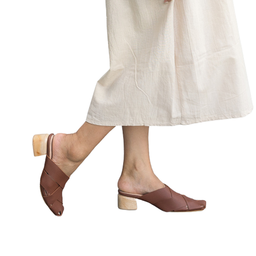 Tan leather heeled mules with wide woven leather upper by Seminyak Leather Bali, providing a custom fit. 5 cm wooden block heel in a natural finish. Leather sole with nonslip rubber for confident steps. A blend of style and comfort for elevated fashion.