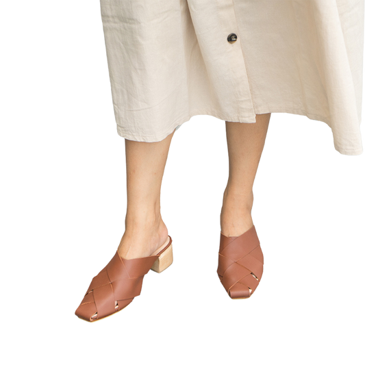 Tan leather heeled mules with wide woven leather upper by Seminyak Leather Bali, providing a custom fit. 5 cm wooden block heel in a natural finish. Leather sole with nonslip rubber for confident steps. A blend of style and comfort for elevated fashion.